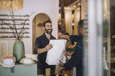 Smiling bearded salesman giving bag to male customer at boutique - MASF38690