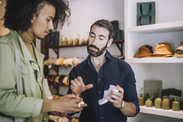 Bearded salesman discussing over shoe with young male customer - MASF38696