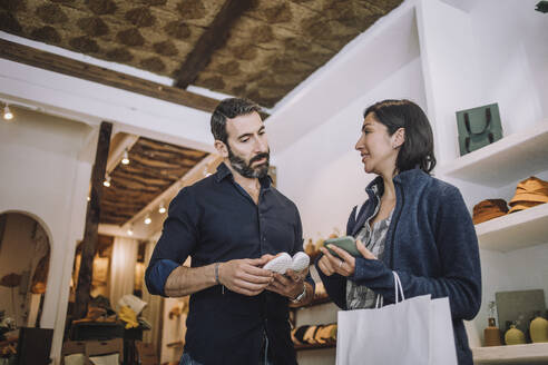 Salesman and female customer discussing over shoe in clothing store - MASF38697