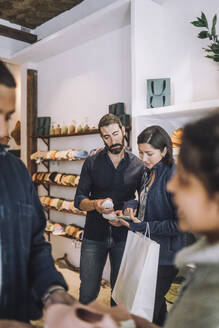 Female customer sharing smart phone with salesman at fashion boutique - MASF38699