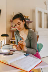 Young woman using glucometer while doing homework at table - MASF38711