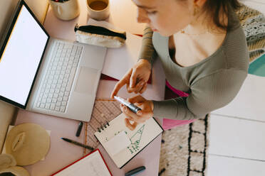 High angle view of young woman using glucometer while doing homework at table - MASF38712