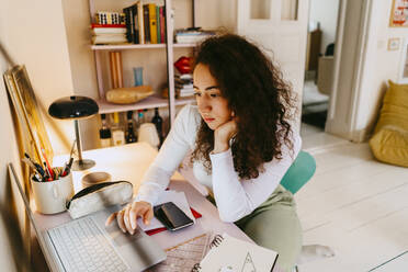 Young woman with curly hair using laptop while studying at home - MASF38715