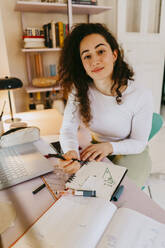 Porträt einer jungen Frau mit lockigem Haar, die am Schreibtisch Hausaufgaben macht - MASF38716