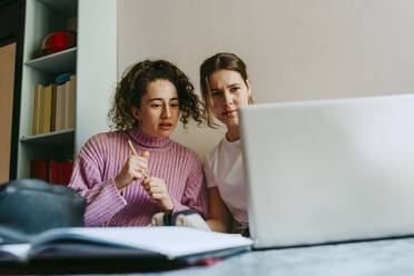 Young female friends looking at laptop while doing homework together - MASF38720