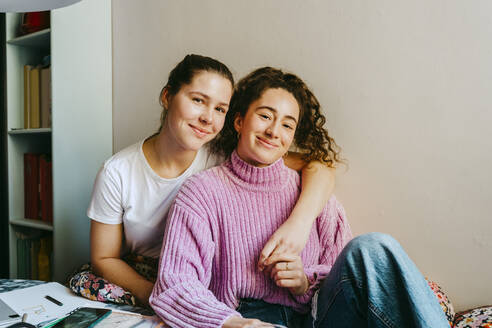 Portrait of smiling young woman with arm around friend sitting at home - MASF38729
