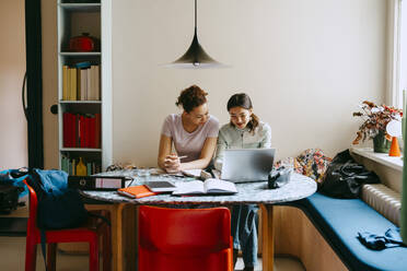 Female friends studying together while using laptop at table - MASF38741