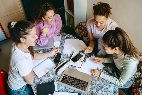 High angle view of female friends discussing while studying together at home - MASF38745