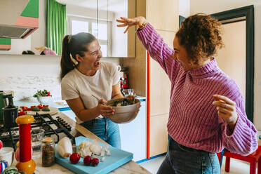 Playful young female friends enjoying while making salad in kitchen at home - MASF38755