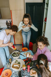 High angle view of woman photographing friends enjoying lunch at home - MASF38757