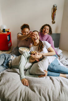 Playful female friends watching TV while enjoying snacks at home - MASF38762