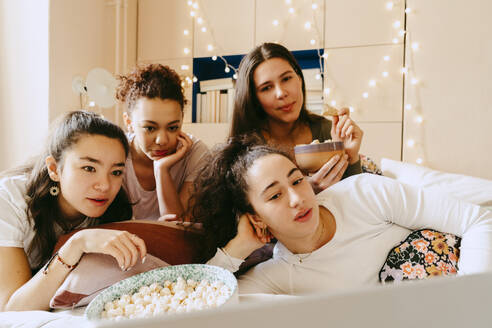 Multiracial female friends watching movie together on laptop at home - MASF38775