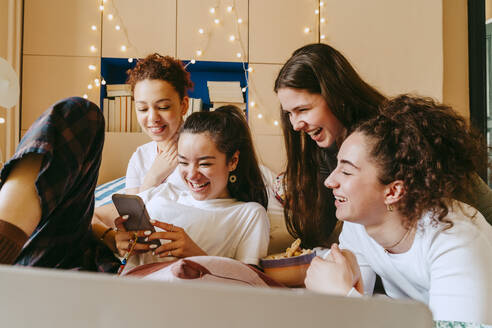 Happy young woman showing smart phone to female friends at home - MASF38781