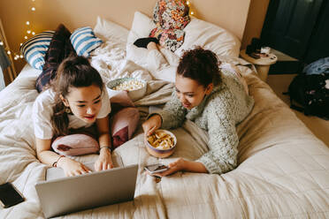 Friends using laptop while lying on bed at home - MASF38784