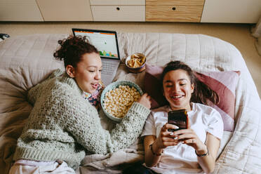 Happy female friends with smart phone and laptop spending leisure time at home - MASF38789