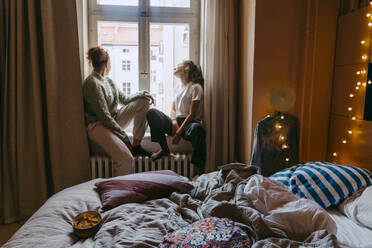 Young female friends sitting at window in bedroom - MASF38793