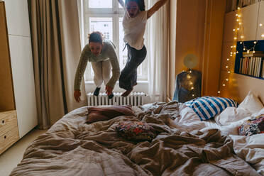 Carefree female friends jumping on bed at home - MASF38796