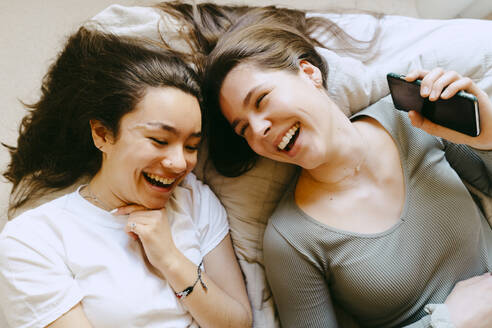 Happiness female friends lying on bed at home - MASF38797