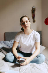 Portrait of young woman sitting on bed at home - MASF38804