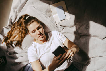 Directly above shot of young woman using smart phone while lying on bed at home - MASF38806