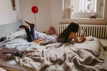 Young woman using mobile phone while lying on bed at home - MASF38811