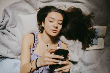 Directly above shot of woman using smart phone while lying on bed at home - MASF38813