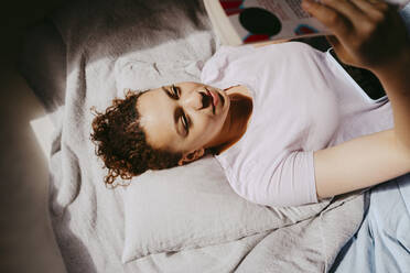 High angle view of teenage girl reading book while lying on bed at home - MASF38817