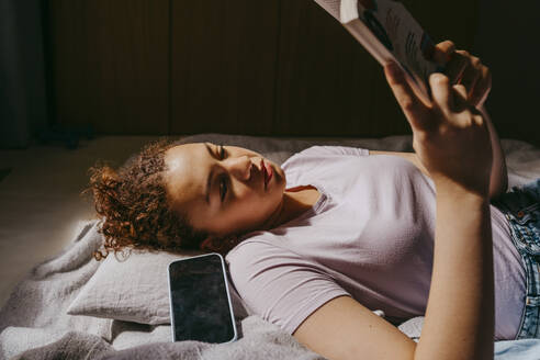 Teenage girl reading book while lying on bed - MASF38818