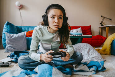 Woman wearing headset playing video game in living room at home - MASF38830