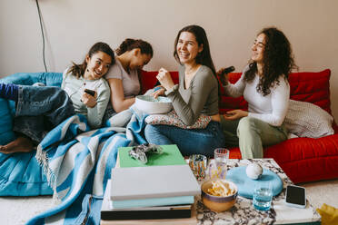 Happy young female friends sitting on sofa at home - MASF38835