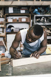 Male entrepreneur marking on wood while upcycling at workshop - MASF38849