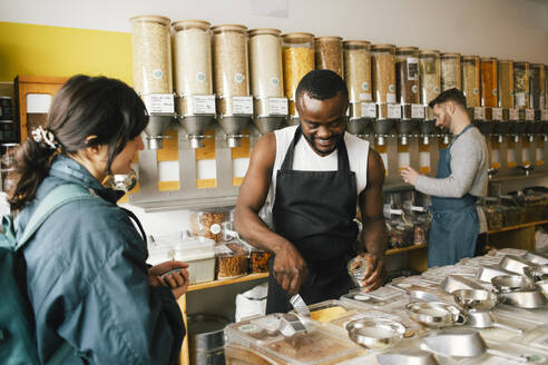 Smiling male owner talking with customer while working in food store - MASF38861