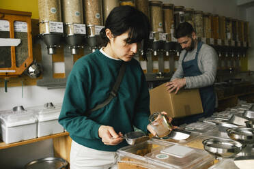 Woman filling jar with food while shopping in organic store - MASF38866