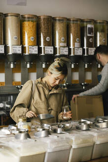 Young woman filling food in container while shopping sustainable store - MASF38868