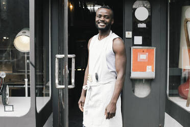 Portrait of happy shop owner standing at entrance - MASF38872