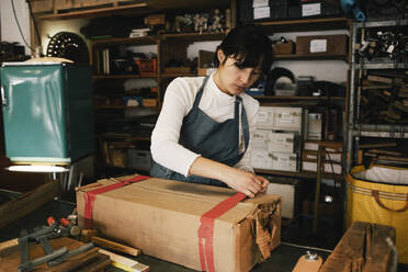 Female entrepreneur opening cardboard box in workshop - MASF38881