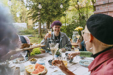 Lächelnde nicht-binäre Person genießt mit Freunden während einer Dinnerparty im Hinterhof - MASF38925