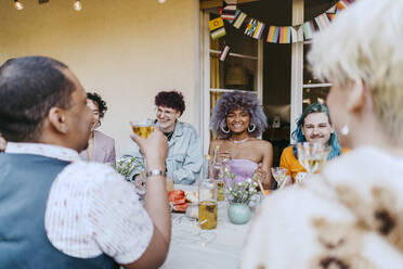 Smiling friends of LGBTQ community enjoying wine during dinner party in back yard - MASF38968