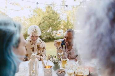 Happy gay friends laughing while having drinks with friends during dinner party in back yard - MASF38973