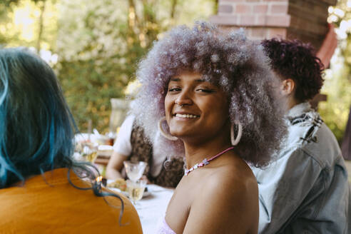 Seitenansicht Porträt einer lächelnden Transfrau mit lockigem Haar während einer Dinnerparty im Hinterhof - MASF38977