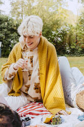 Smiling gay man with blanket sitting in back yard during dinner party - MASF38992