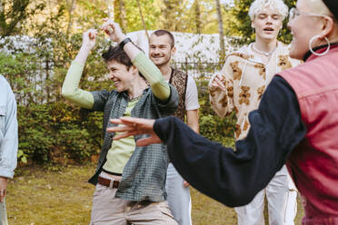 Happy non-binary person dancing amidts LGBTQ friends during party in back yard - MASF39002