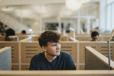 Smiling young man looking away while sitting in library at university - MASF39009