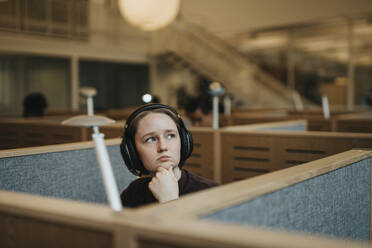 Thoughtful young student sitting with hand on chin in library at university - MASF39011