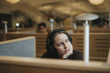 Contemplative young female student with hand on chin in library at university - MASF39014