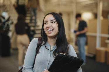 Cheerful female student carrying file folder at university - MASF39033