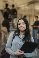 Portrait of confident female student carrying file folder standing in university - MASF39034