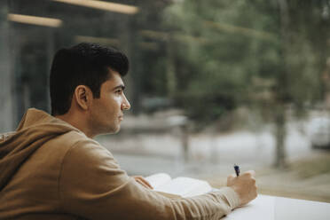 Thoughtful young male student studying at table in university - MASF39035