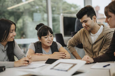 Smiling students and professor discussing at table in university - MASF39049