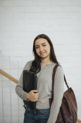 Porträt einer selbstbewussten Studentin mit einer Mappe, die an der Wand einer Universität steht - MASF39057